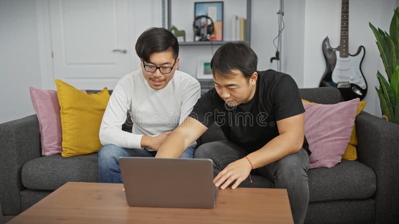 Dos amigos hombres asiáticos que usan una laptop en una sala de estar moderna fotografía de archivo libre de regalías