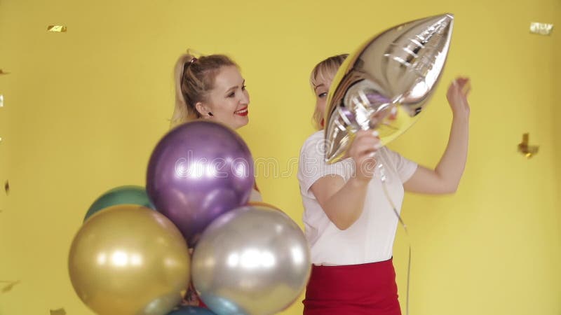 Dos amigos rubios sosteniendo globos coloridos y bailando