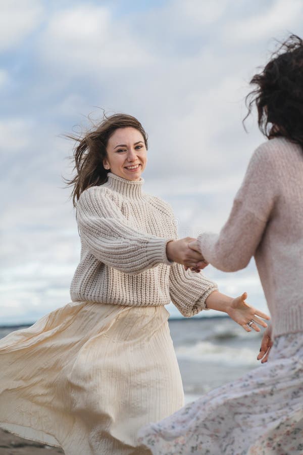 Dos amigos se divierten y disfrutan la vida. las hermanas bailan y ríen mucho. chicas en sudaderas cálidas con un tejido grande imagenes de archivo