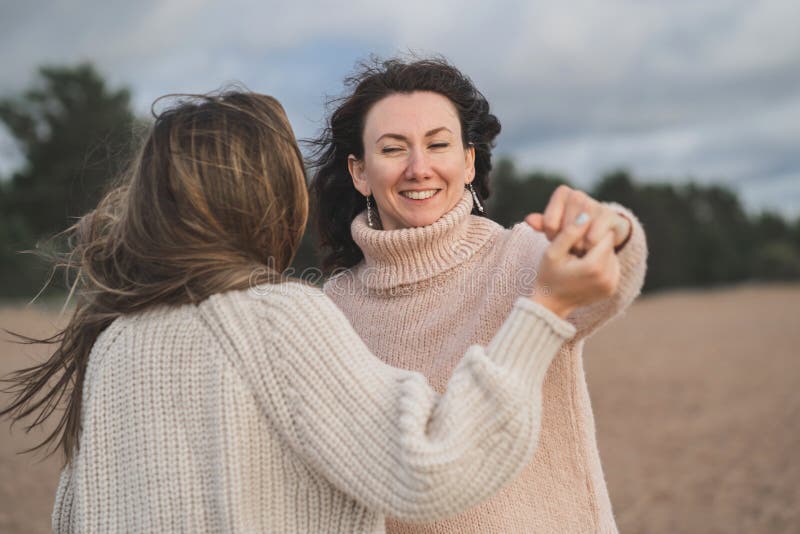 Dos amigos se divierten y disfrutan la vida. las hermanas bailan y ríen mucho. chicas en sudaderas cálidas con un tejido grande imagen de archivo