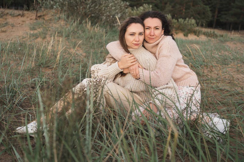 Dos amigos íntimos abrazan suavemente. hermanas en cálidos jersey disfrutan de la naturaleza. dos brunettes se sientan sobre el cé fotos de archivo