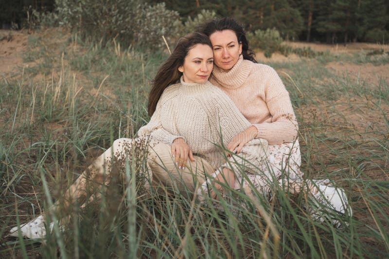 Dos amigos íntimos abrazan suavemente. hermanas en cálidos jersey disfrutan de la naturaleza. dos brunettes se sientan sobre el cé foto de archivo