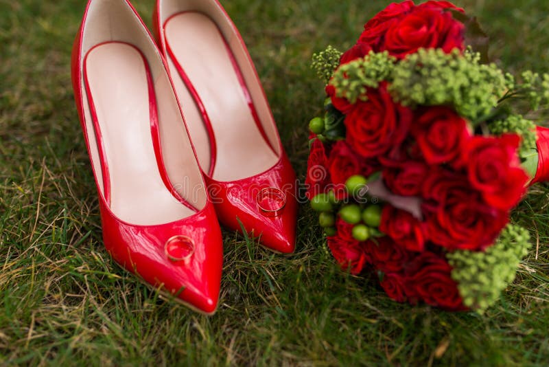 Dos anillos de bodas de oro mienten en los zapatos femeninos de la moda roja en hierba verde boda imagen de archivo libre de regalías Dos anillos de bodas de oro mienten en los zapatos femeninos de la moda roja en hierba verde boda imagen de archivo libre de regalías