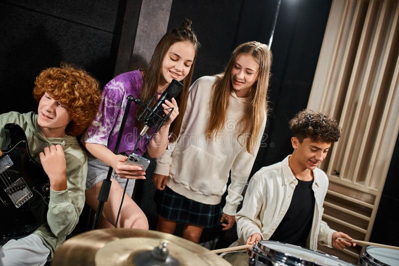 two pretty teenage girls singing and looking at lyrics on phone while boys playing drums and guitar, stock photo. two pretty teenage girls singing and looking at lyrics on phone while boys playing drums and guitar, stock photo