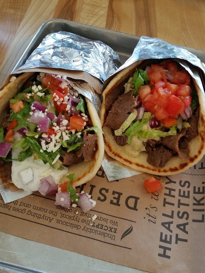Dos bocadillos griegos del girocompás. Dos bocadillos frescos del girocompás envueltos para arriba con los tomates, carne, cebolla, lechuga, queso feta, en una pita con la hoja en una bandeja