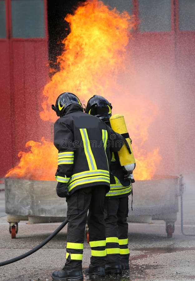 Dos bomberos durante el ejercicio con un fuego del depósito lleno y un t imagenes de archivo Dos bomberos durante el ejercicio con un fuego del depósito lleno y un t imagenes de archivo