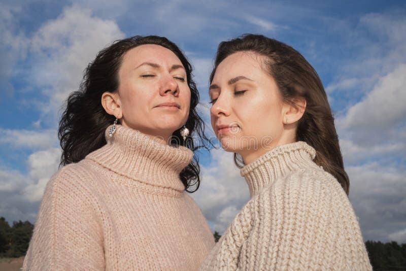 Dos brunetas con los ojos cerrados sueñan. chicas contra el cielo con nubes. chicas hermosas en sudaderas cálidas. fotografía de archivo libre de regalías