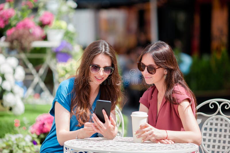 Dos chicas jóvenes en el café del aire libre Dos mujeres después de hacer compras con los bolsos que se sientan en café al aire l imagen de archivo Dos chicas jóvenes en el café del aire libre Dos mujeres después de hacer compras con los bolsos que se sientan en café al aire l imagen de archivo