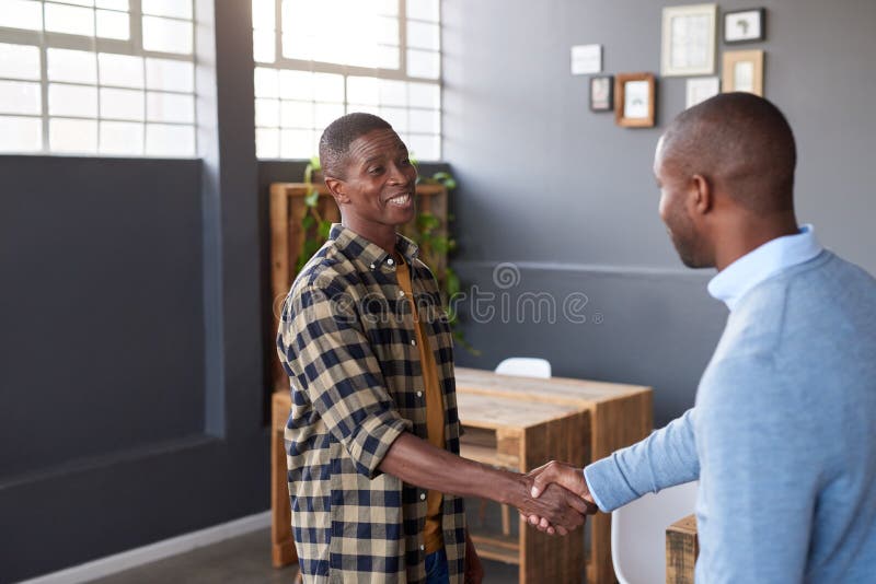 Dos compañeros de trabajo africanos sonrientes que sacuden las manos juntas en una oficina imagenes de archivo Dos compañeros de trabajo africanos sonrientes que sacuden las manos juntas en una oficina imagenes de archivo