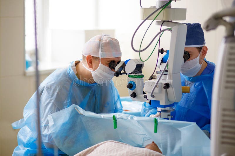 Dos doctores realizan una operación en los ojos, científicos miran a través de un microscopio, el paciente se acuestan, mucho pro fotografía de archivo Dos doctores realizan una operación en los ojos, científicos miran a través de un microscopio, el paciente se acuestan, mucho pro fotografía de archivo