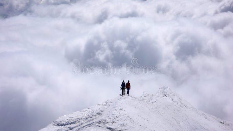 Dos escaladores de montaña femeninos en un canto estrecho de la cumbre alto sobre los bancos de nube en los valles abajo fotos de archivo Dos escaladores de montaña femeninos en un canto estrecho de la cumbre alto sobre los bancos de nube en los valles abajo fotos de archivo