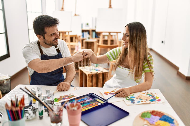 Dos estudiantes sonriendo con los puños de bulto alegres sentados sobre la mesa en la escuela de arte fotos de archivo libres de regalías