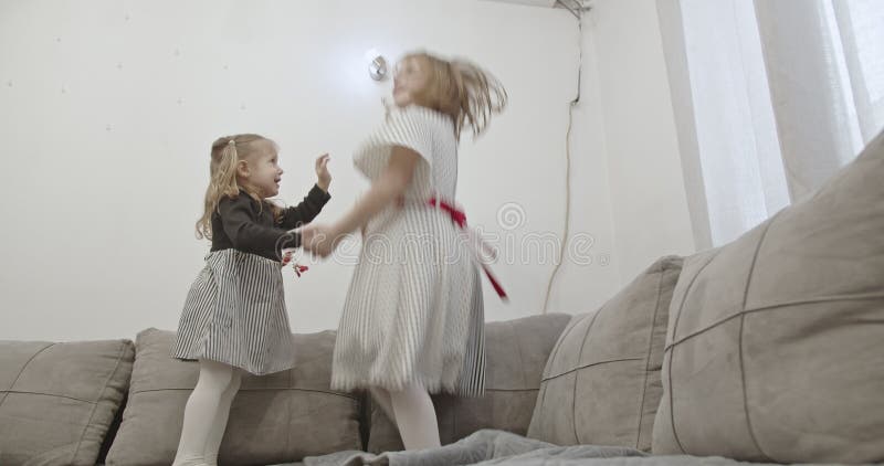 Dos hermanas felices saltando y jugando juntas en un sofá disfrutando de un tiempo familiar de calidad en casa metrajes