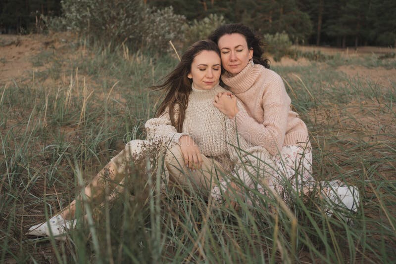 Dos hermanas sentadas sobre el césped con los ojos cerrados y abrazadas. las brunetas disfrutan de una hermosa naturaleza y entre fotos de archivo