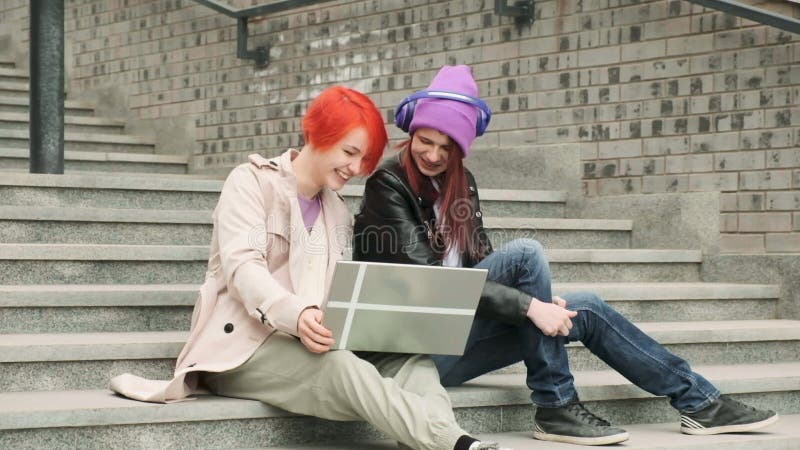 Dos hermosos amigos jóvenes están sentados y usando un portátil para el entretenimiento