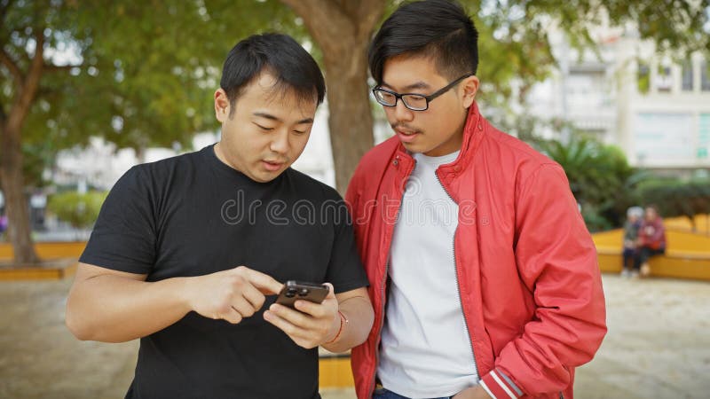 Dos hombres asiáticos que usan smartphone en un parque fotografía de archivo