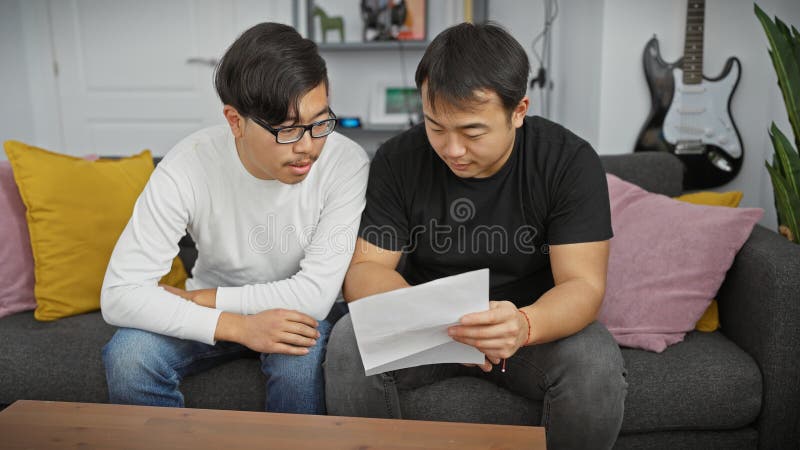 Dos hombres asiáticos revisan un documento juntos en una sala de estar moderna que refleja amistad o colaboración imagen de archivo