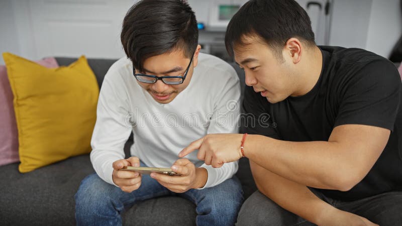 Dos hombres asiáticos se unen con un smartphone en un moderno salón de apartamentos imágenes de archivo libres de regalías