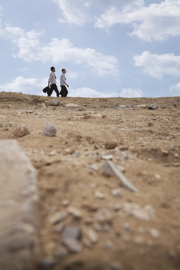 Dos hombres de negocios jovenes que caminan a través del desierto, en la distancia foto de archivo Dos hombres de negocios jovenes que caminan a través del desierto, en la distancia foto de archivo