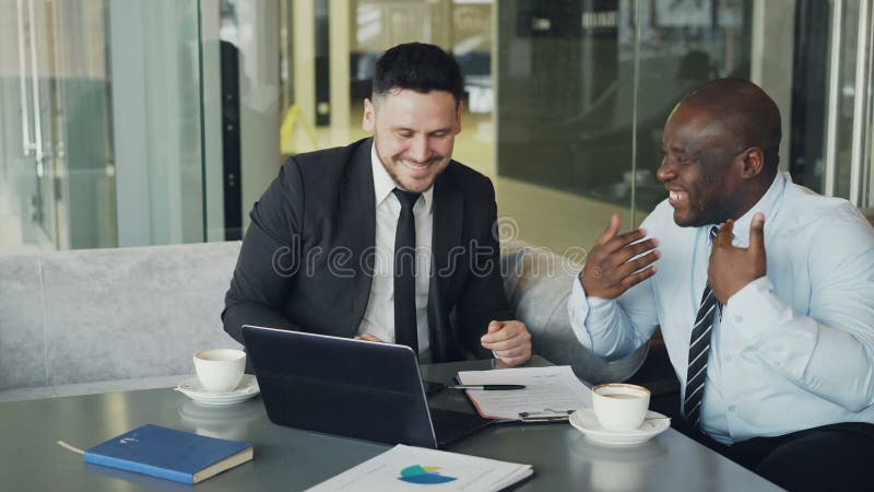 Dos hombres de negocios que hablan el ANG que ríe en café moderno Colegas del negocio que se divierten y que bromean mirando el o