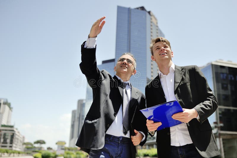 Dos hombres de negocios que trabajan sobre un nuevo proyecto sobre los edificios de oficinas del fondo foto de archivo Dos hombres de negocios que trabajan sobre un nuevo proyecto sobre los edificios de oficinas del fondo foto de archivo