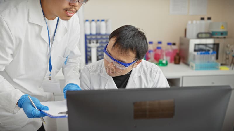 Dos hombres en gabinetes de laboratorio usando computadora en un ambiente de laboratorio científico imagen de archivo libre de regalías