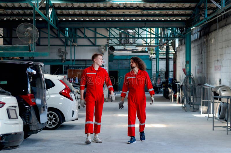 Dos hombres mecánicos guapos con uniforme rojo que caminan por fila de vehículo en el taller mecánico del garaje amigo trabajan ju imágenes de archivo libres de regalías