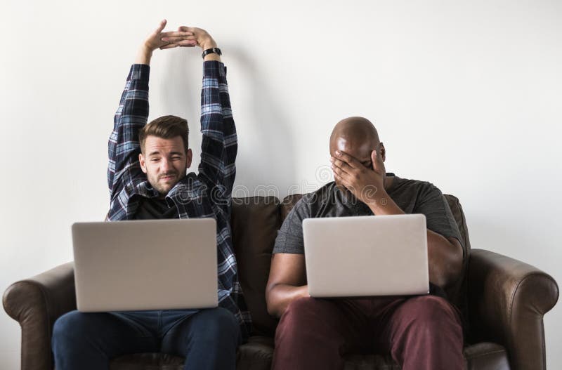 Dos hombres que usan el ordenador portátil en el sofá imagen de archivo Dos hombres que usan el ordenador portátil en el sofá imagen de archivo