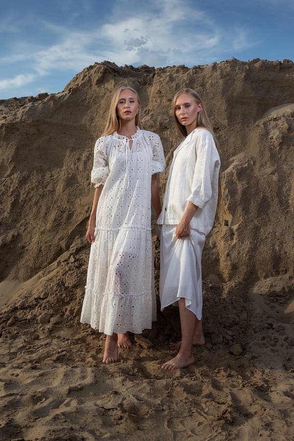 Dos jóvenes hermanas gemelas atractivas posando en cantera de arena con elegantes ropas blancas imagen de archivo libre de regalías