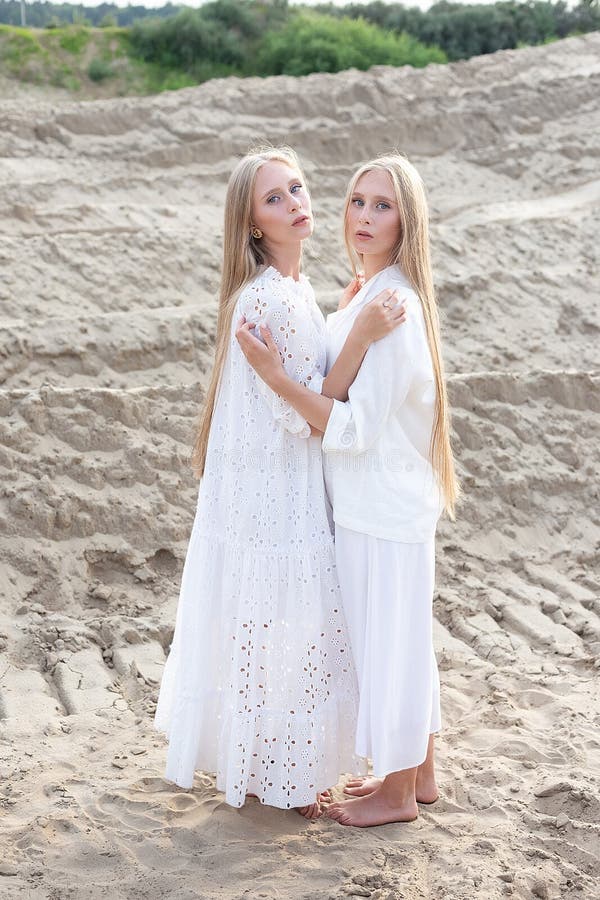 Dos jóvenes hermanas gemelas atractivas posando en cantera de arena con elegantes ropas blancas foto de archivo libre de regalías