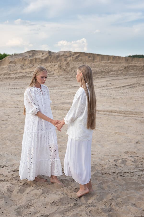 Dos jóvenes hermanas gemelas atractivas posando en cantera de arena con elegantes ropas blancas foto de archivo libre de regalías