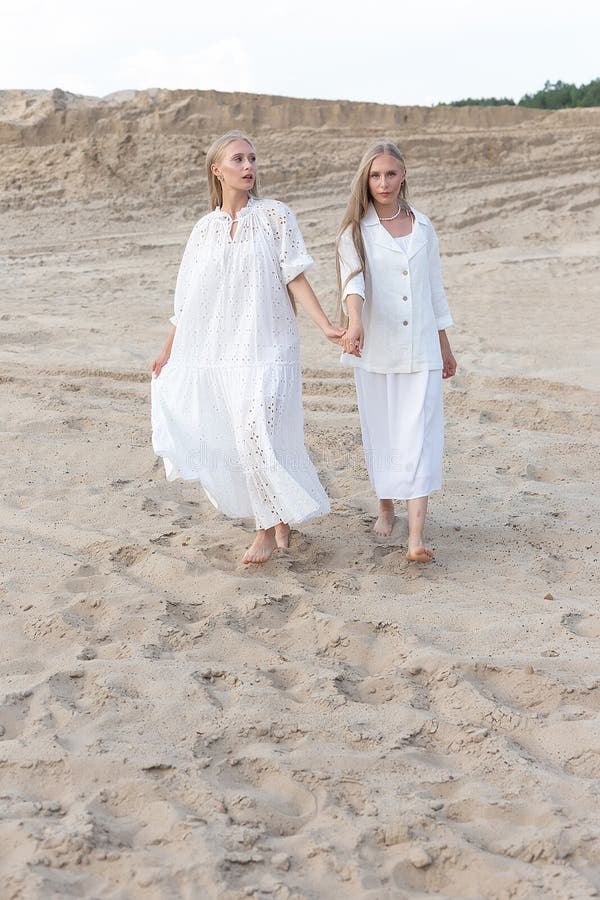 Dos jóvenes hermanas gemelas atractivas posando en cantera de arena con elegantes ropas blancas. Dos jóvenes y lindos gemelos con largo pelo rubio posando en cantera de arena con elegante chaqueta de falda de vestir blanco. sesión fotográfica de verano de moda elegante. hermanas idénticas pasan tiempo juntas al aire libre