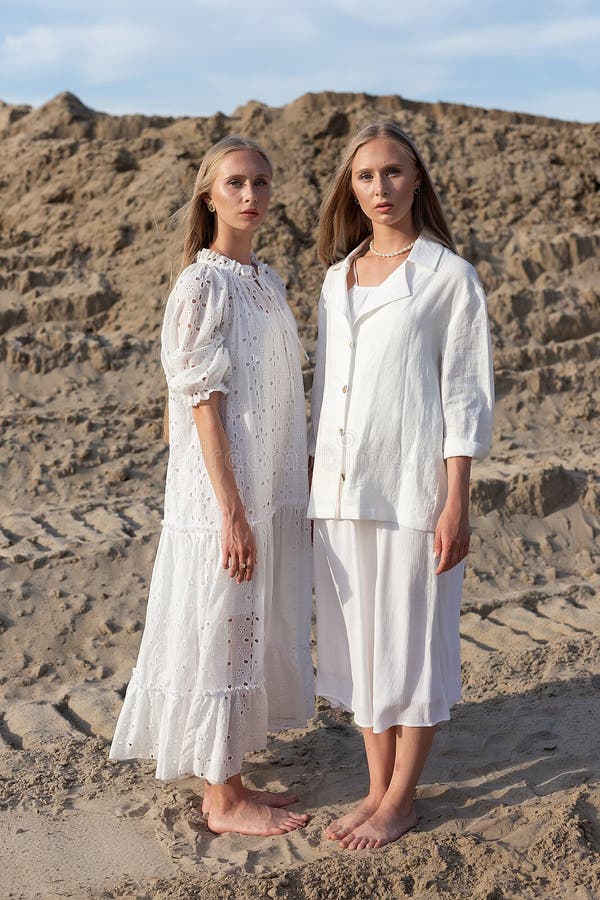 Dos jóvenes hermanas gemelas atractivas posando en cantera de arena con elegantes ropas blancas fotografía de archivo libre de regalías