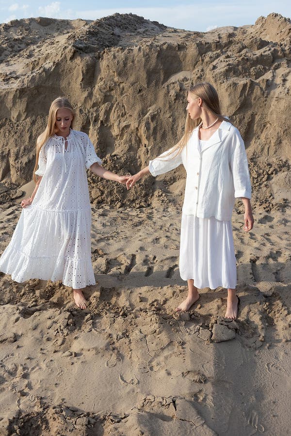 Dos jóvenes hermanas gemelas atractivas posando en cantera de arena con elegantes ropas blancas foto de archivo