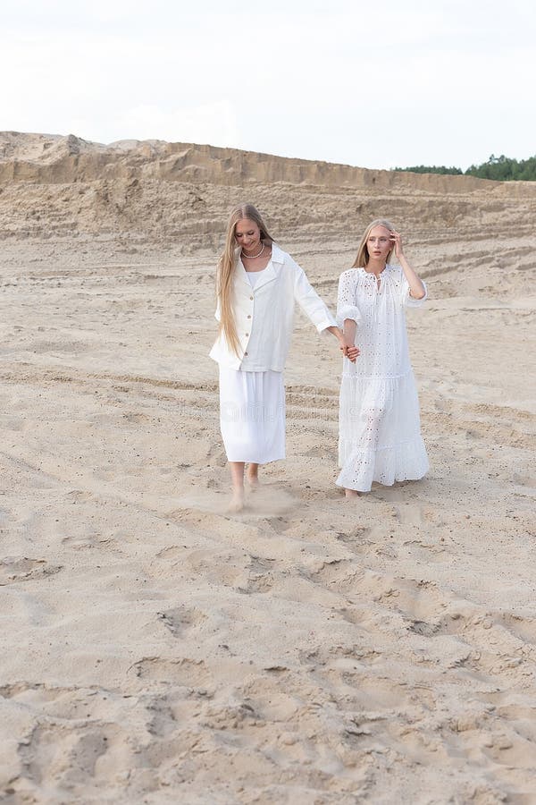 Dos jóvenes hermanas gemelas atractivas posando en cantera de arena con elegantes ropas blancas foto de archivo