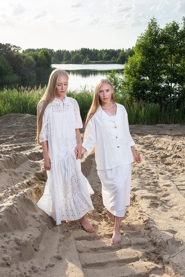 Dos jóvenes hermanas gemelas atractivas posando en la playa de arena con elegantes ropas blancas fotos de archivo libres de regalías