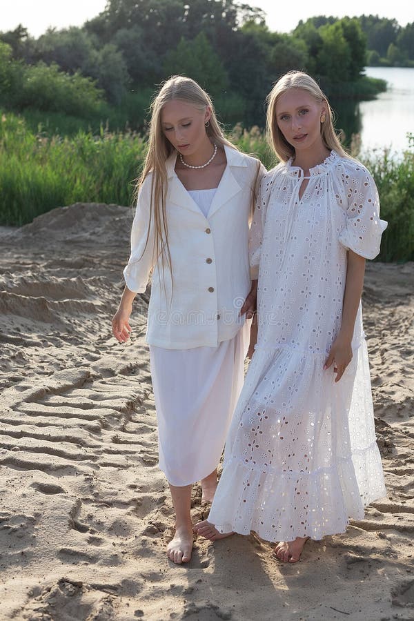 Dos jóvenes hermanas gemelas atractivas posando en la playa de arena con elegantes ropas blancas foto de archivo libre de regalías