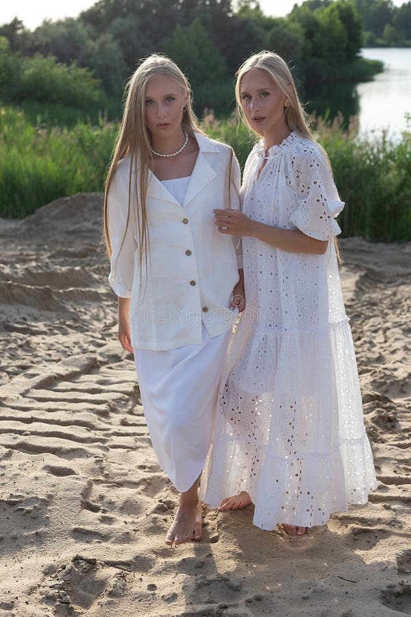 Dos jóvenes hermanas gemelas atractivas posando en la playa de arena con elegantes ropas blancas fotos de archivo libres de regalías