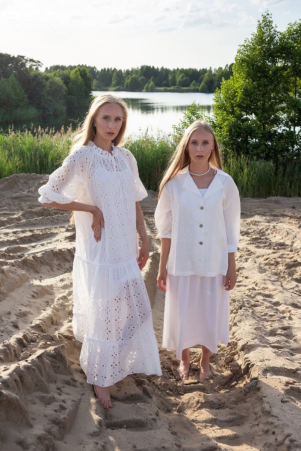 Dos jóvenes hermanas gemelas atractivas posando en la playa de arena con elegantes ropas blancas imagen de archivo