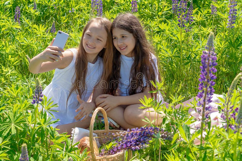 Dos muchachas adolescentes hacen el selfie en un teléfono entre las flores en un campo en un día soleado imagenes de archivo Dos muchachas adolescentes hacen el selfie en un teléfono entre las flores en un campo en un día soleado imagenes de archivo