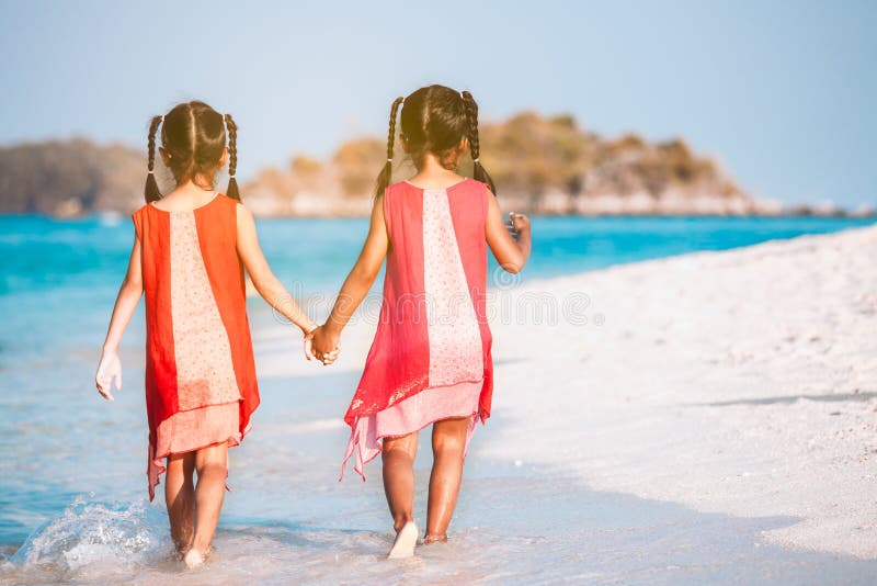 Dos muchachas asiáticas del niño que llevan a cabo la mano y que caminan junto en la playa cerca del mar en vacaciones de veran fotos de archivo libres de regalías Dos muchachas asiáticas del niño que llevan a cabo la mano y que caminan junto en la playa cerca del mar en vacaciones de veran fotos de archivo libres de regalías