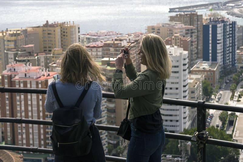 Dos muchachas se colocan en una colina y una mirada en el panorama hermoso de la ciudad española de Málaga en un caliente fotografía de archivo libre de regalías Dos muchachas se colocan en una colina y una mirada en el panorama hermoso de la ciudad española de Málaga en un caliente fotografía de archivo libre de regalías