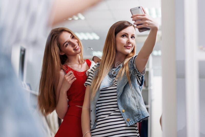 Dos muchachas sonrientes que toman el selfie mientras que hace compras en una tienda de ropa fotografía de archivo Dos muchachas sonrientes que toman el selfie mientras que hace compras en una tienda de ropa fotografía de archivo