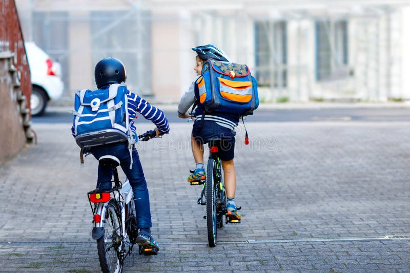 Two school kid boys in safety helmet riding with bike in the city with backpacks. Happy children in colorful clothes biking on bicycles on way to school. Safe way for kids outdoors to school. Two school kid boys in safety helmet riding with bike in the city with backpacks. Happy children in colorful clothes biking on bicycles on way to school. Safe way for kids outdoors to school.