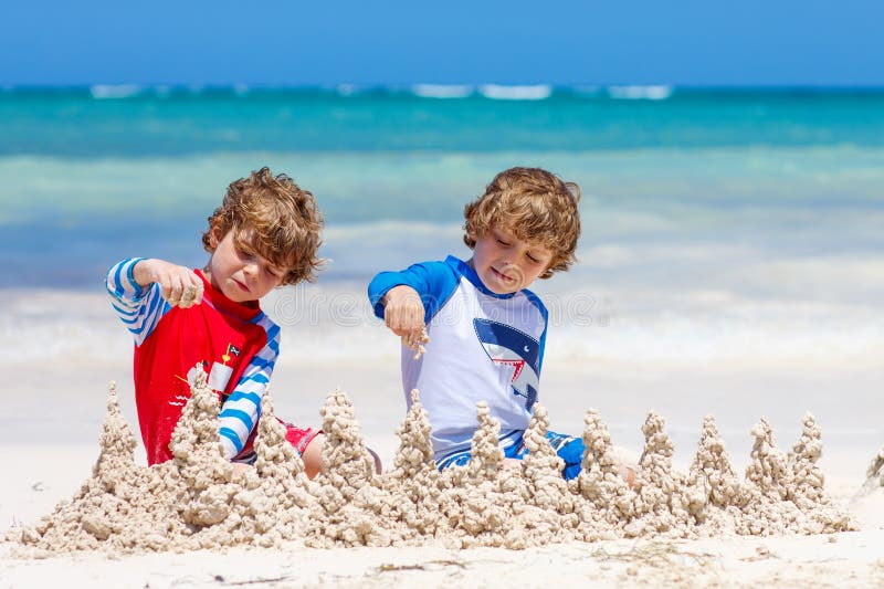 Dos muchachos del niño que construyen la arena se escudan en la playa tropical foto de archivo libre de regalías Dos muchachos del niño que construyen la arena se escudan en la playa tropical foto de archivo libre de regalías