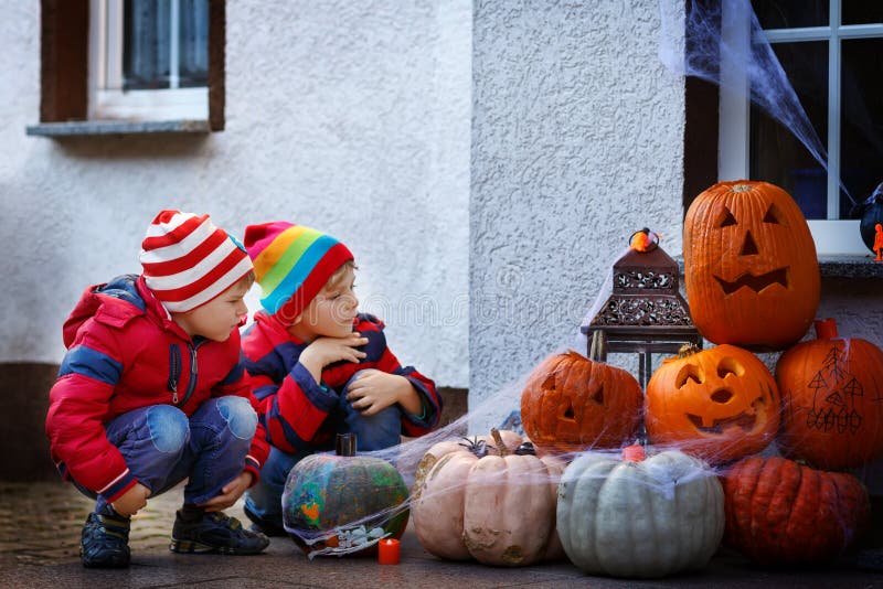 Dos muchachos del niño que se sientan con las calabazas tradicionales de las Jack-o-linternas para Halloween por la puerta asusta imagen de archivo libre de regalías Dos muchachos del niño que se sientan con las calabazas tradicionales de las Jack-o-linternas para Halloween por la puerta asusta imagen de archivo libre de regalías