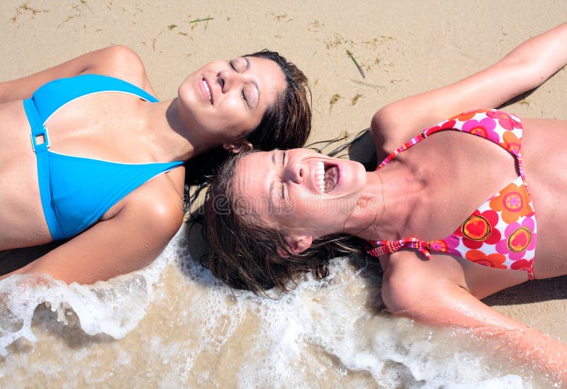 Dos mujeres atractivas jovenes salpicaron por la onda fría en la playa imagen de archivo libre de regalías Dos mujeres atractivas jovenes salpicaron por la onda fría en la playa imagen de archivo libre de regalías