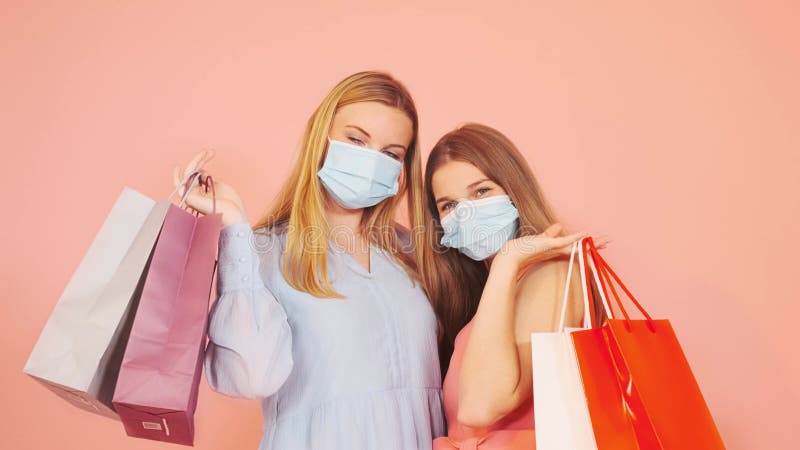 Dos mujeres con bolsas de compras y divirtiéndose juntas en un fondo rosado