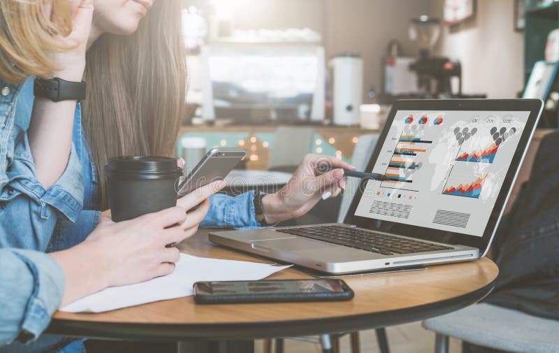 Dos mujeres de negocios jovenes que se sientan en la tabla en café, café de consumición y hablar Primera pluma y smartphone de te imagen de archivo Dos mujeres de negocios jovenes que se sientan en la tabla en café, café de consumición y hablar Primera pluma y smartphone de te imagen de archivo