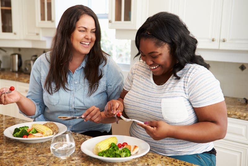 Dos mujeres gordas en dieta que comen la comida sana en cocina